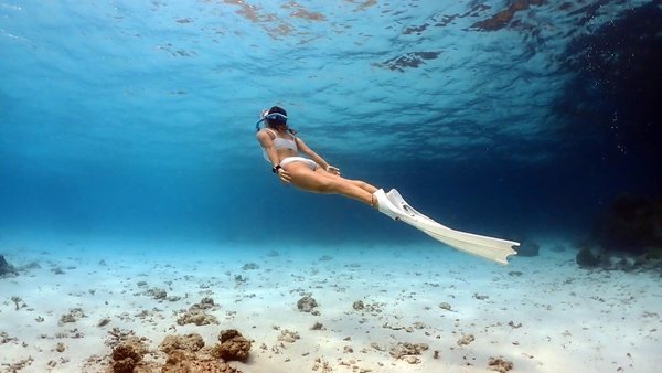 Freediver gliding calmly over a sandy bottom with long fins