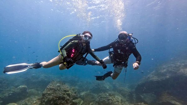 Two supervised scuba divers swimming together over a reef